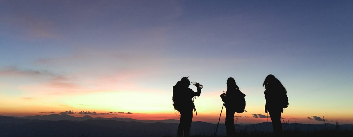 three people hiking in the dark against a sunset
