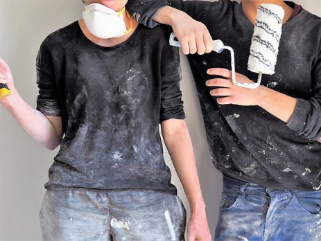 two people covered in paint, holding a roller and a hammer, after decorating.